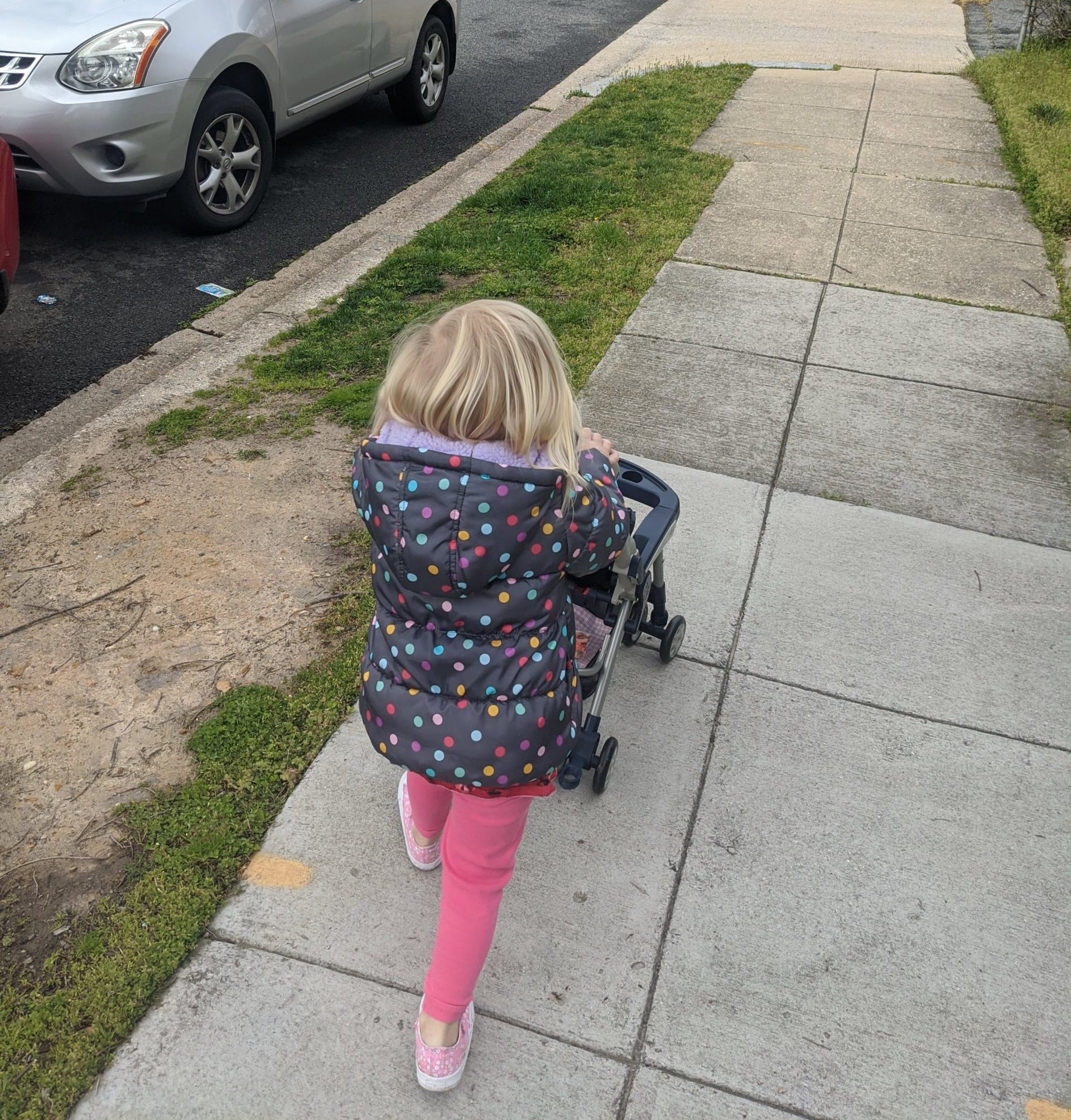 3-year old girl walking down a sidewalk with a toy stroller