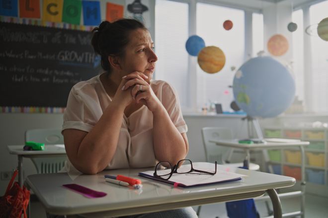 Teacher Sitting Alone at Desk in Empty Classroom